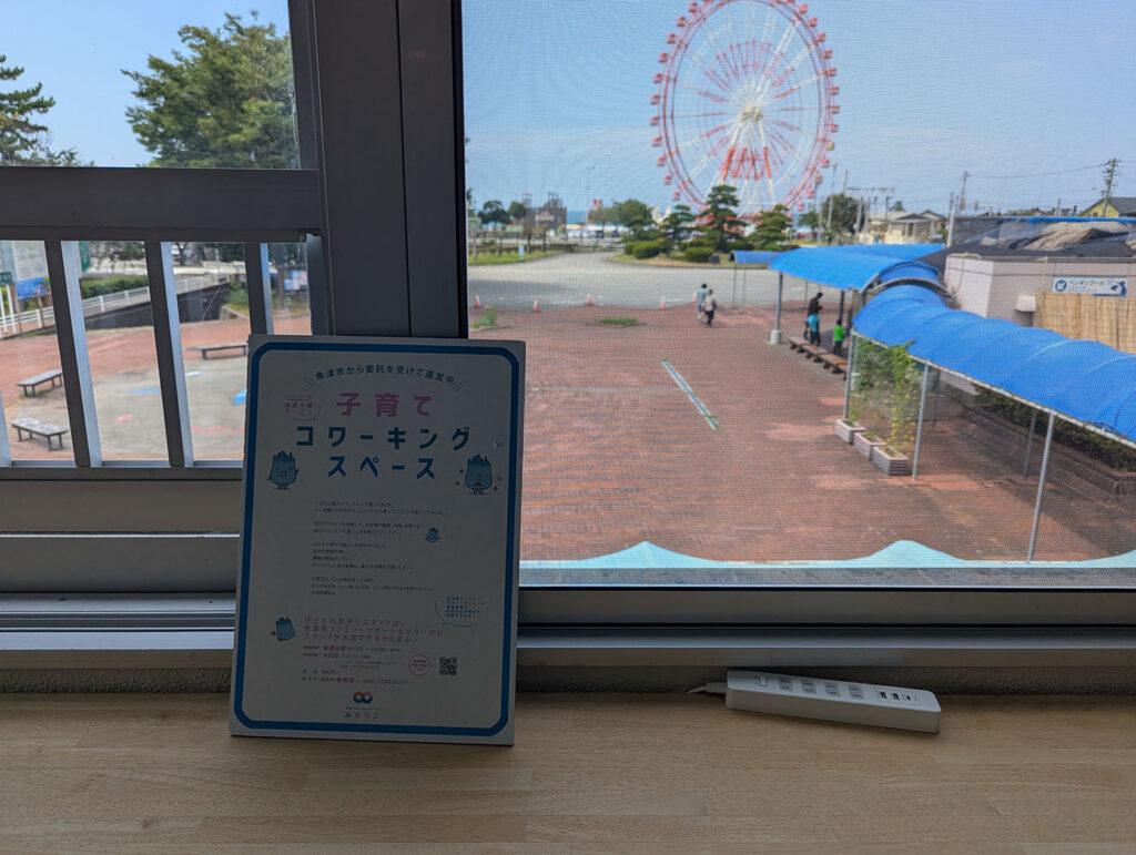 窓辺に置かれた「子育てコワーキングスペース」の案内板。外には観覧車が見える。