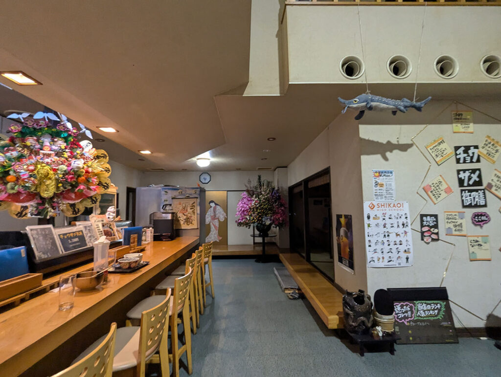 鹿追町「びっくり寿司」の店内。カウンター席の奥に飾られた大きな花輪や、壁に掲げられたチョウザメの飾りとポスターが目を引く。