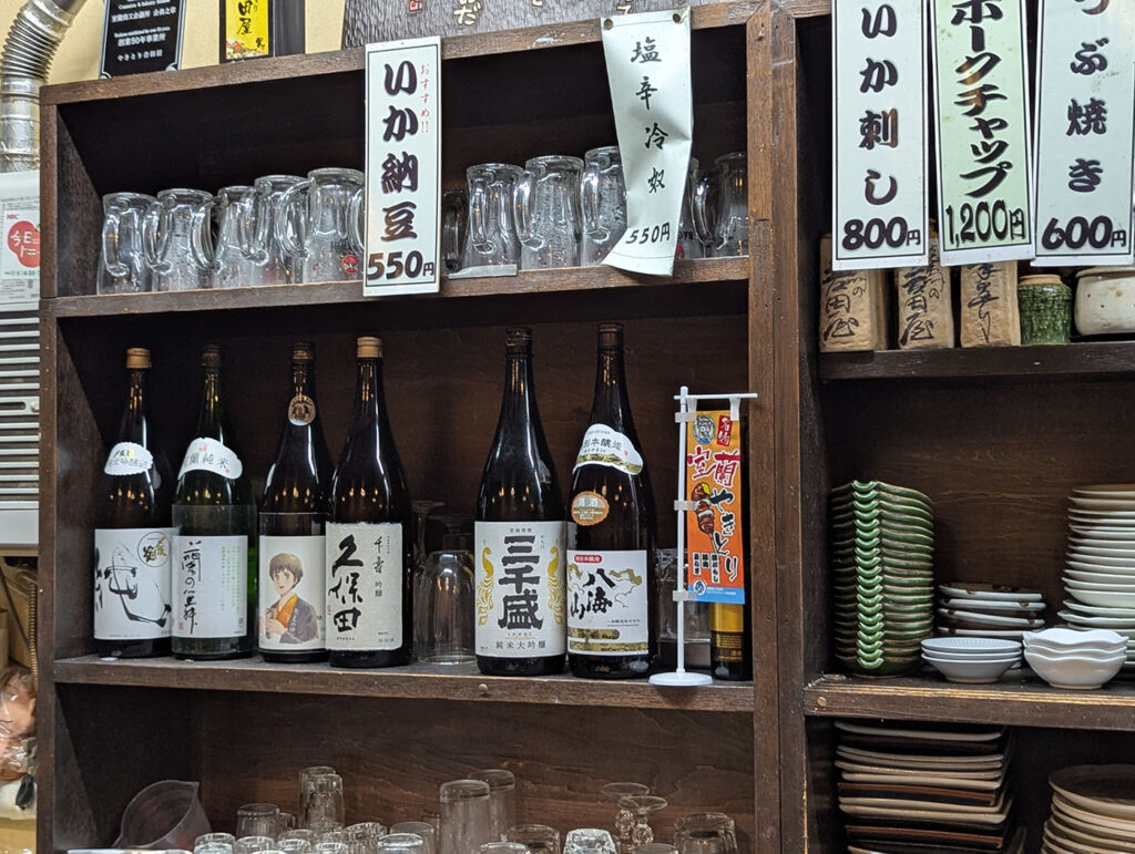 吉田屋店内の棚に並ぶ一升瓶とグラス。室蘭の地酒や全国の銘酒が揃う。