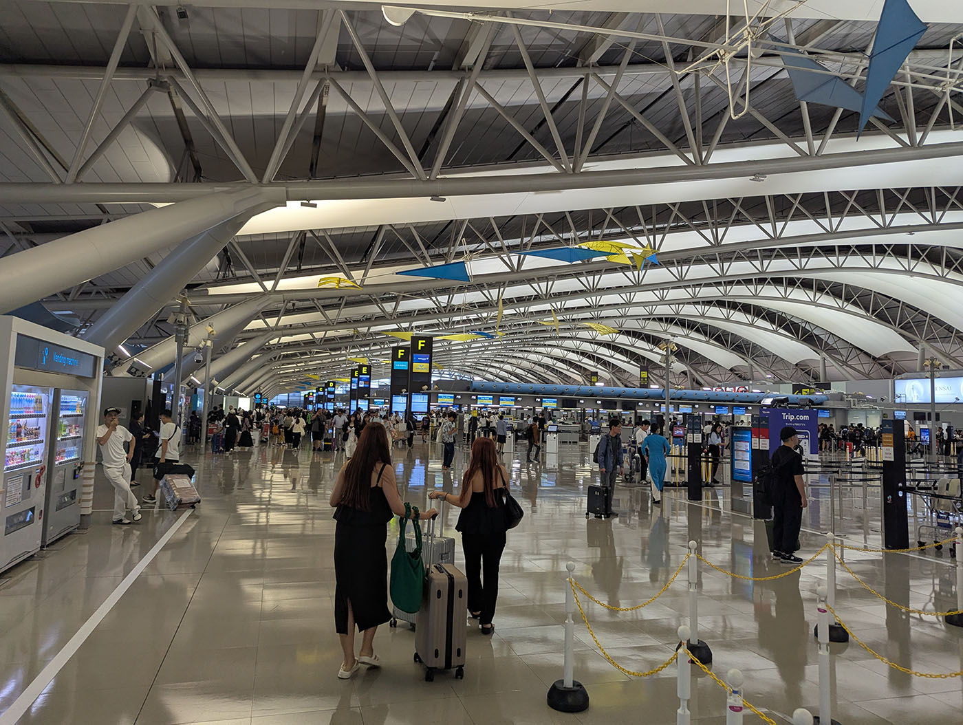 関西国際空港第1ターミナルの出発ロビー。天井のアーチが連なる開放的な空間に、多くの旅行者がチェックインカウンターへ向かっている。