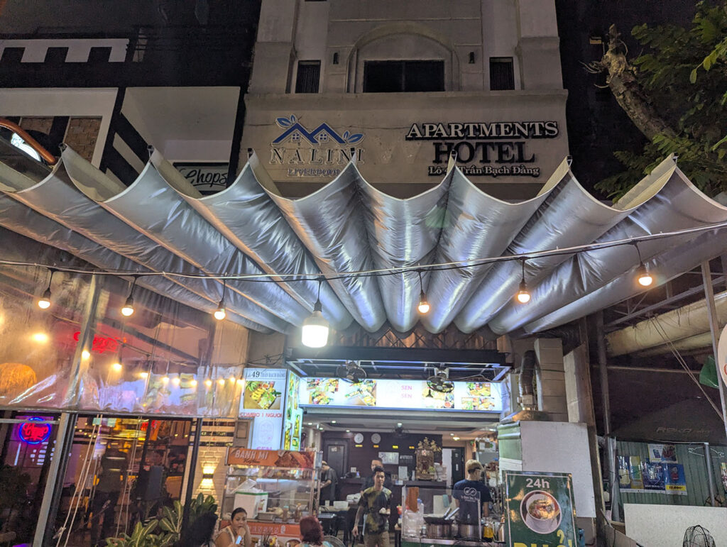 ホテルの1階にある24時間営業の食堂。天井には波型の銀色ダクトがぶら下がり、夜でも明るい照明が路地を照らしている。