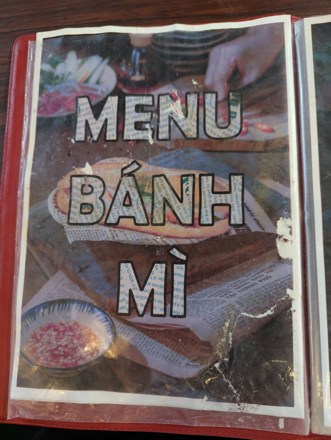 使い込まれたメニュー表の表紙。「MENU BÁNH MÌ」の文字と、バインミーやフォーの写真。