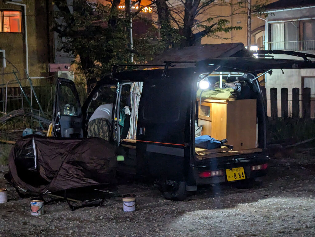夜の境内に停められた軽バン、バックドアが開いて車内が照らされている様子とソロテント