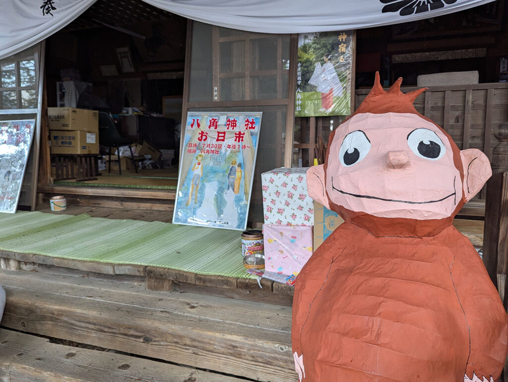 神社の社務所前に置かれたおさるのジョージの張り子人形とイベントポスター