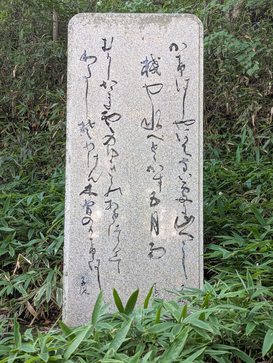 木曽の桟の正岡子規句碑。御影石に草書体で「かけはしやあぶない処に山つつじ」と刻まれた石碑。周囲は草木に囲まれている。