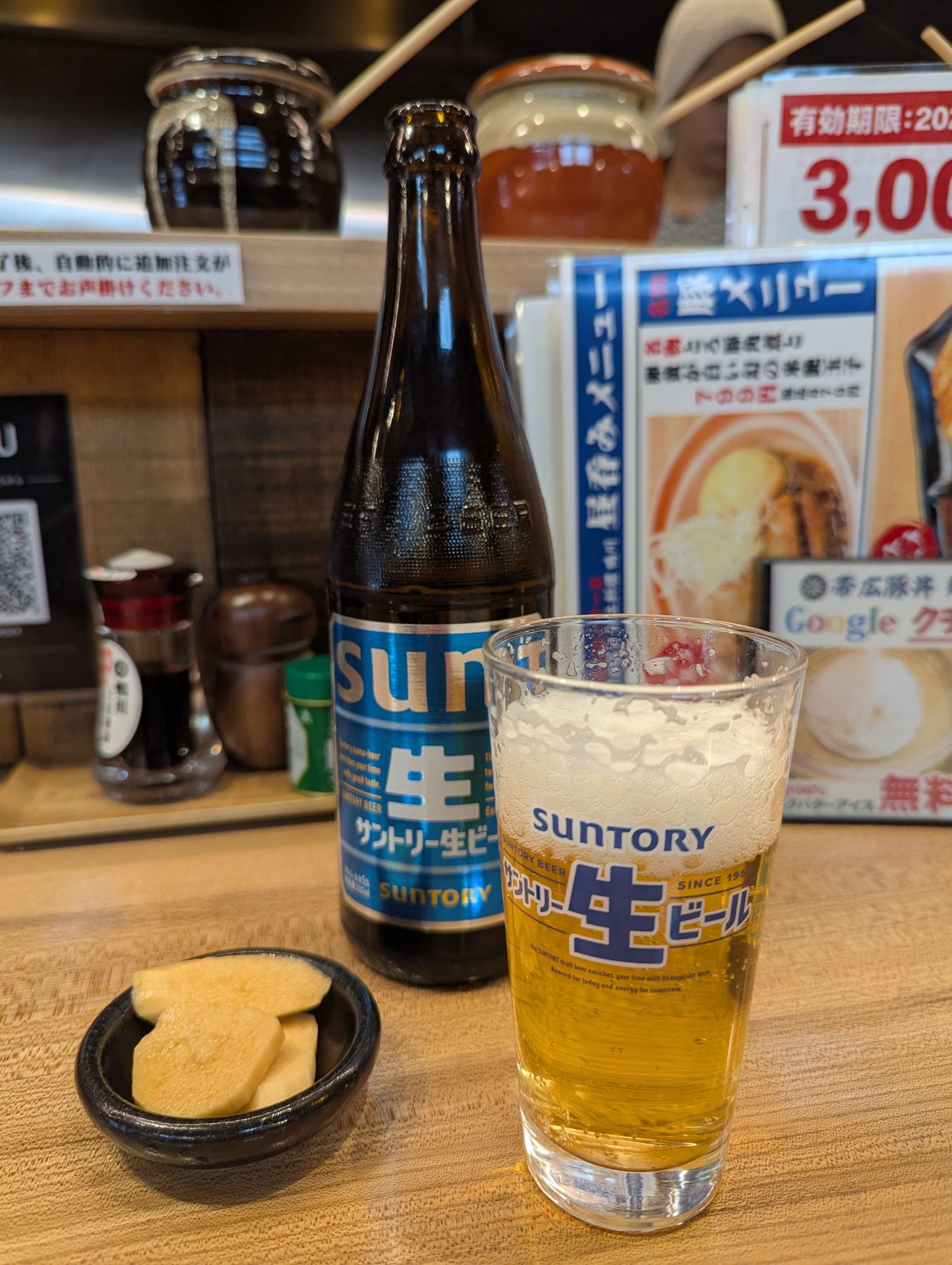 カウンターに置かれたサントリー生ビールと山芋のたまり漬けの小鉢