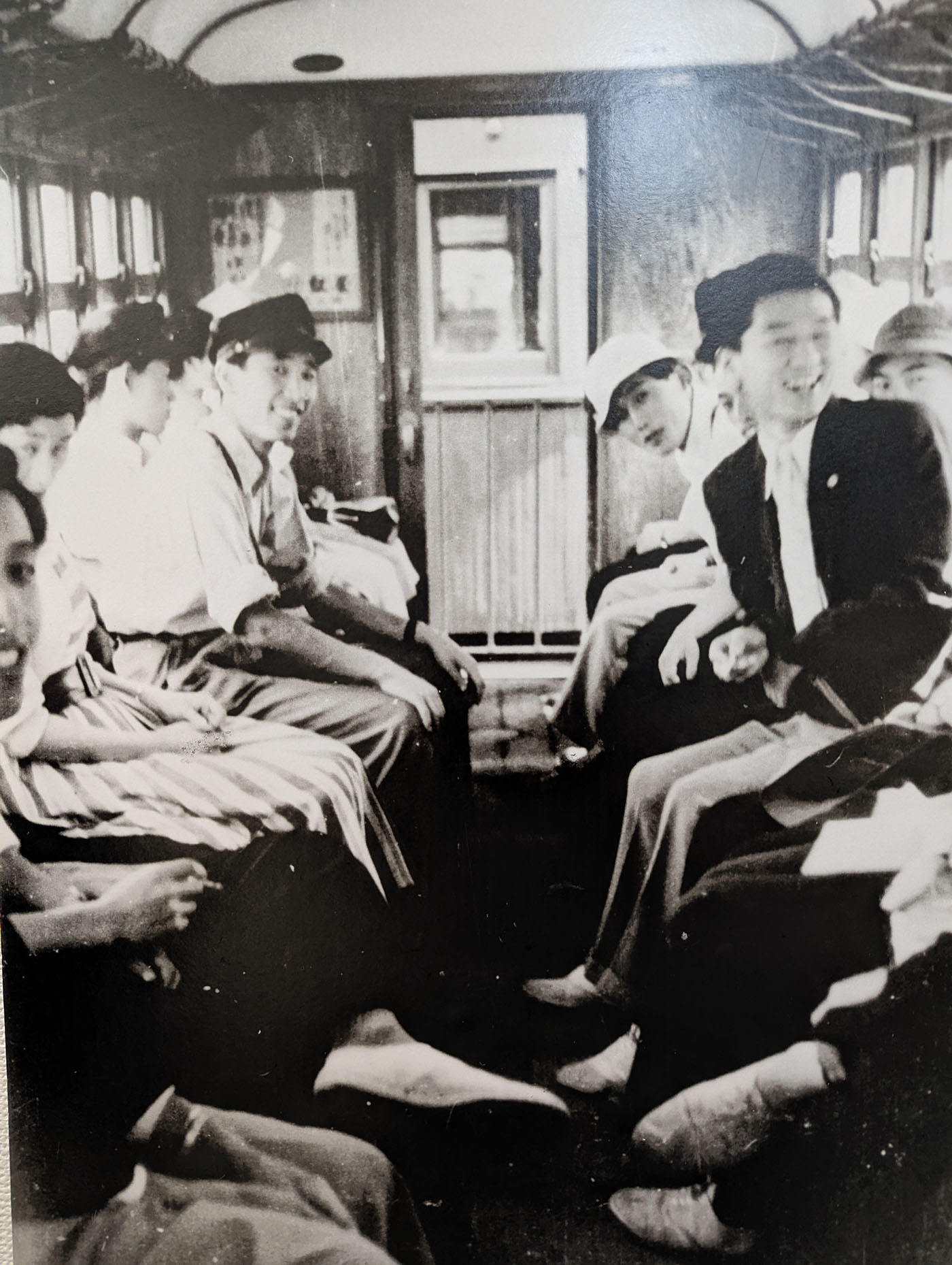 十勝鉄道の車内で笑顔を見せる学生たちのモノクロ写真。木製車両の内部に、通学や移動をしていた当時の空気感が残る。