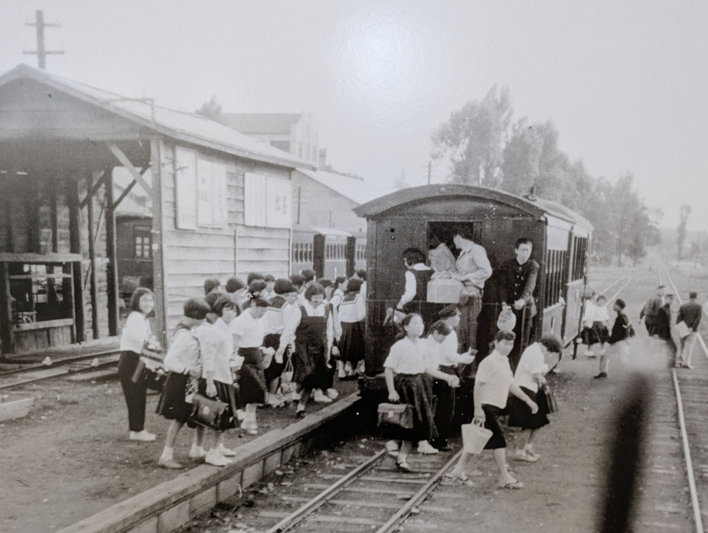 十勝鉄道の駅で列車から降りる学生たちのモノクロ写真。制服姿の子どもたちが線路を渡り、地域の生活鉄道だったことを感じさせる一枚。